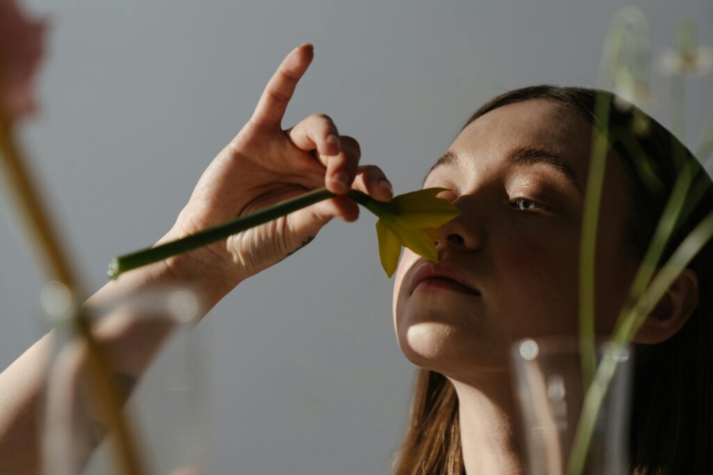 Adult woman gently smelling a daffodil flower indoors, captured in warm natural light.